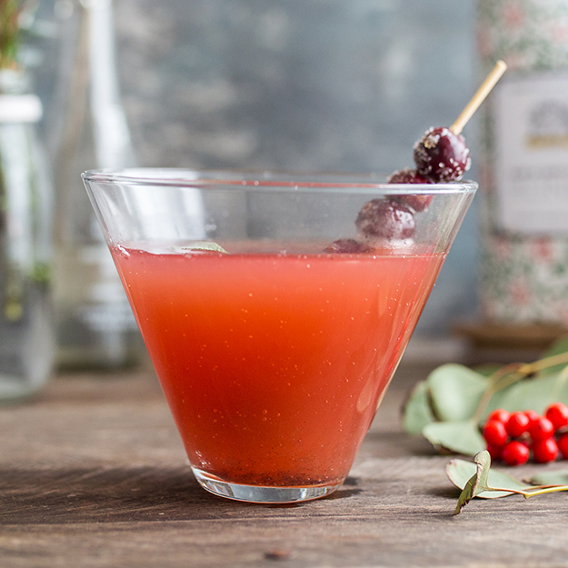 Berry cocktail in a glass with a sugar-coated berry garnish, on a wooden table.