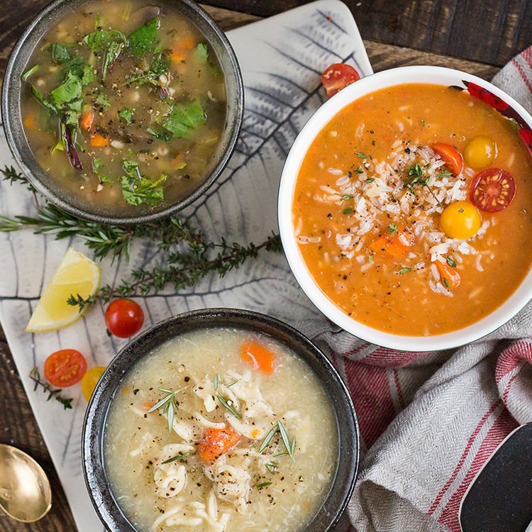 Three bowls of soup: chicken noodle, tomato bisque with rice, and vegetable, on rustic wooden, with fresh ingredients.