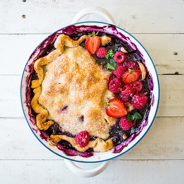 Berry cobbler with crust, with fresh berries on top, on a white wooden surface.