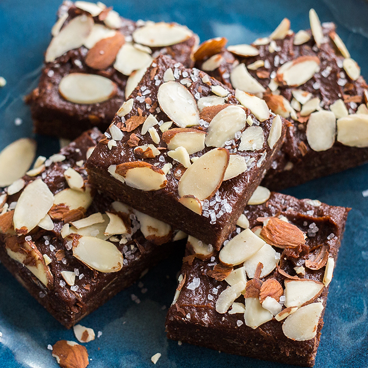 Chocolate brownies with almond slices on a blue plate.