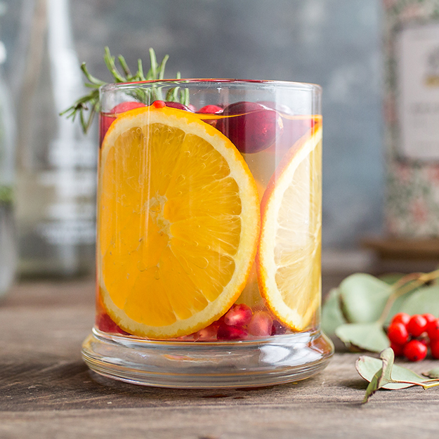 A glass of iced apple cider with apple slice garnish in a clear glass, set against a rustic backdrop.