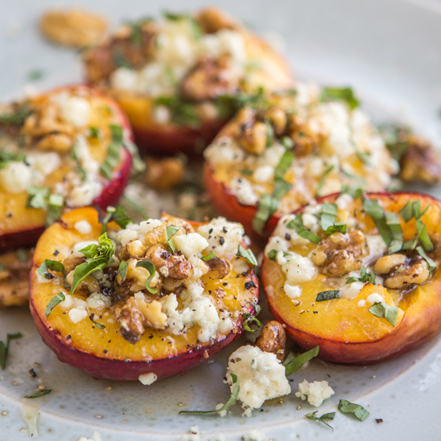 Grilled peach halves with cheese and walnuts, garnished with basil on a plate.