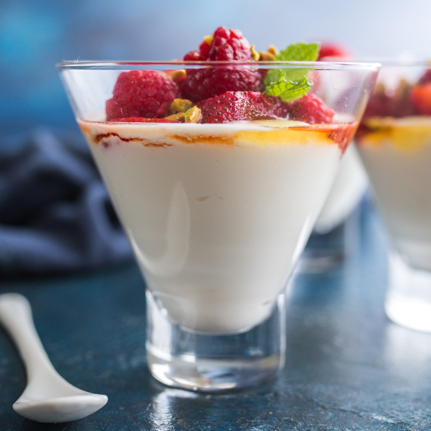 Whipped honey lemon ricotta in a glass with raspberries and pistachios on top.