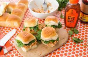 Chicken slider sandwiches, Nate's honey bottle, and rolls on a polka dot tablecloth.