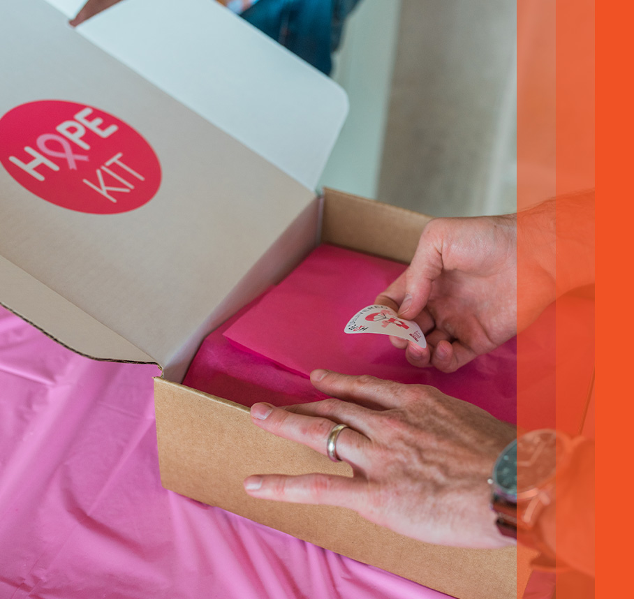 Hands closing a National Breast Cancer Foundation "HOPE KIT" box with pink tissue paper.