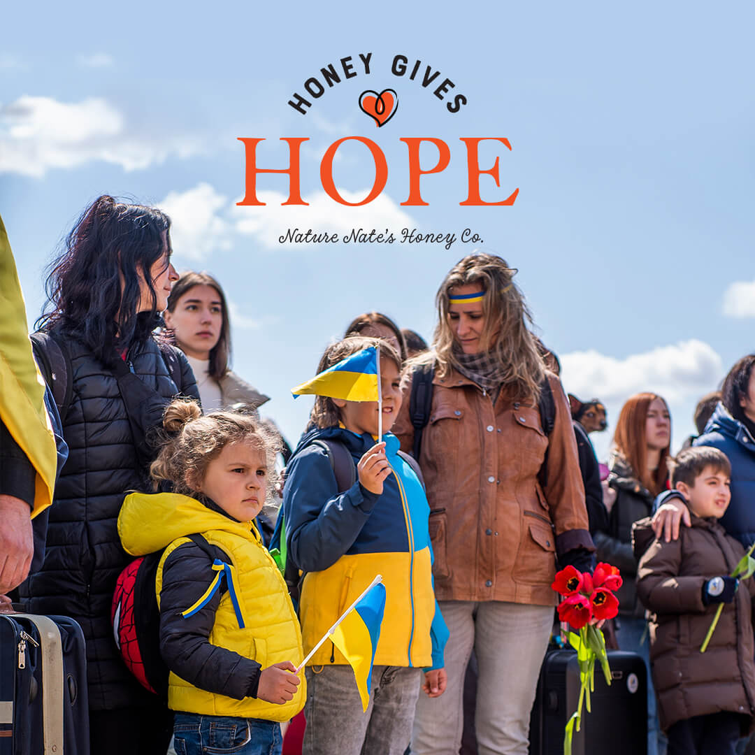 Group of people with two kids holding Ukrainian flags under HONEY GIVES HOPE, Nature Nate's Honey Co. overlay text.