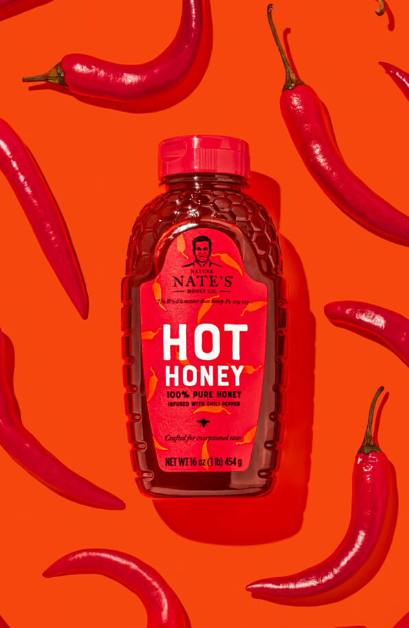 Nate's hot honey bottle displayed in center of array of red chili peppers against an orange background.