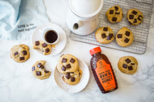 Chocolate chunk cookies on a cooling rack and plate, with coffee, a jug of milk, and Nate's Honey.