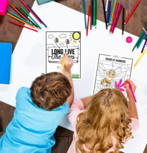 Two children coloring at a table, surrounded by colorful pencils, focusing on a Long Live the Bees, themed coloring page.