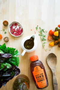 Salad ingredients, dressing, and a Nate's honey bottle on a wooden surface.