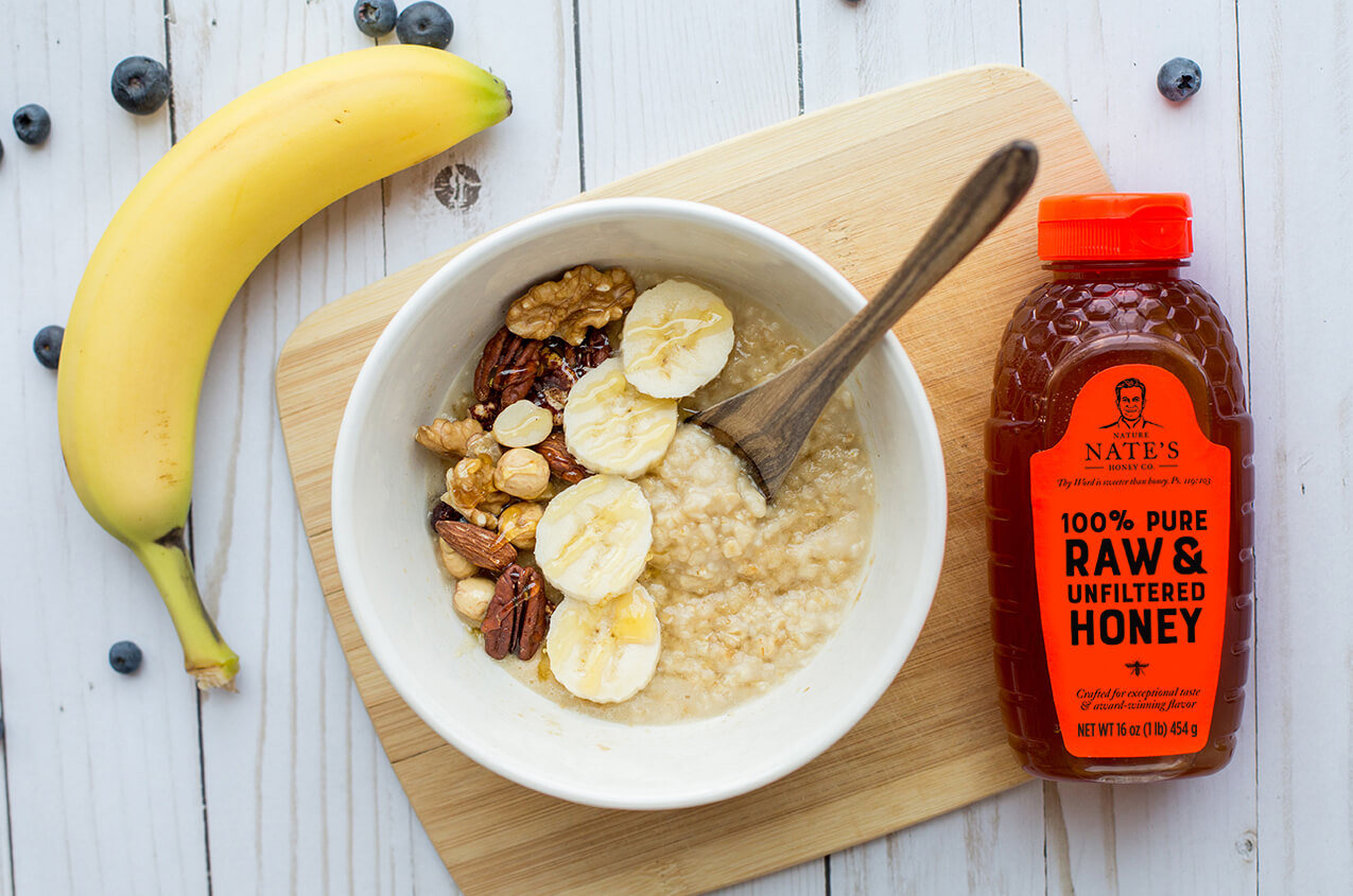 Oatmeal with bananas, nuts, and a bottle of raw honey on a wooden board.
