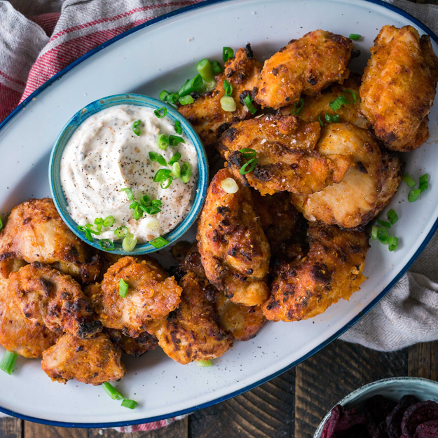Fried chicken wings with dipping sauce, garnished with green onions on a platter.