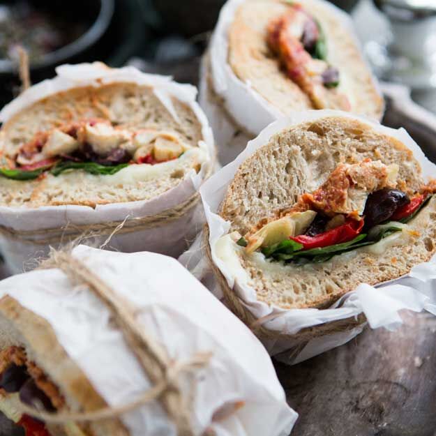 Wrapped muffaletta sandwiches cut in half and wrapped in paper, showing various fillings, on rustic surface.