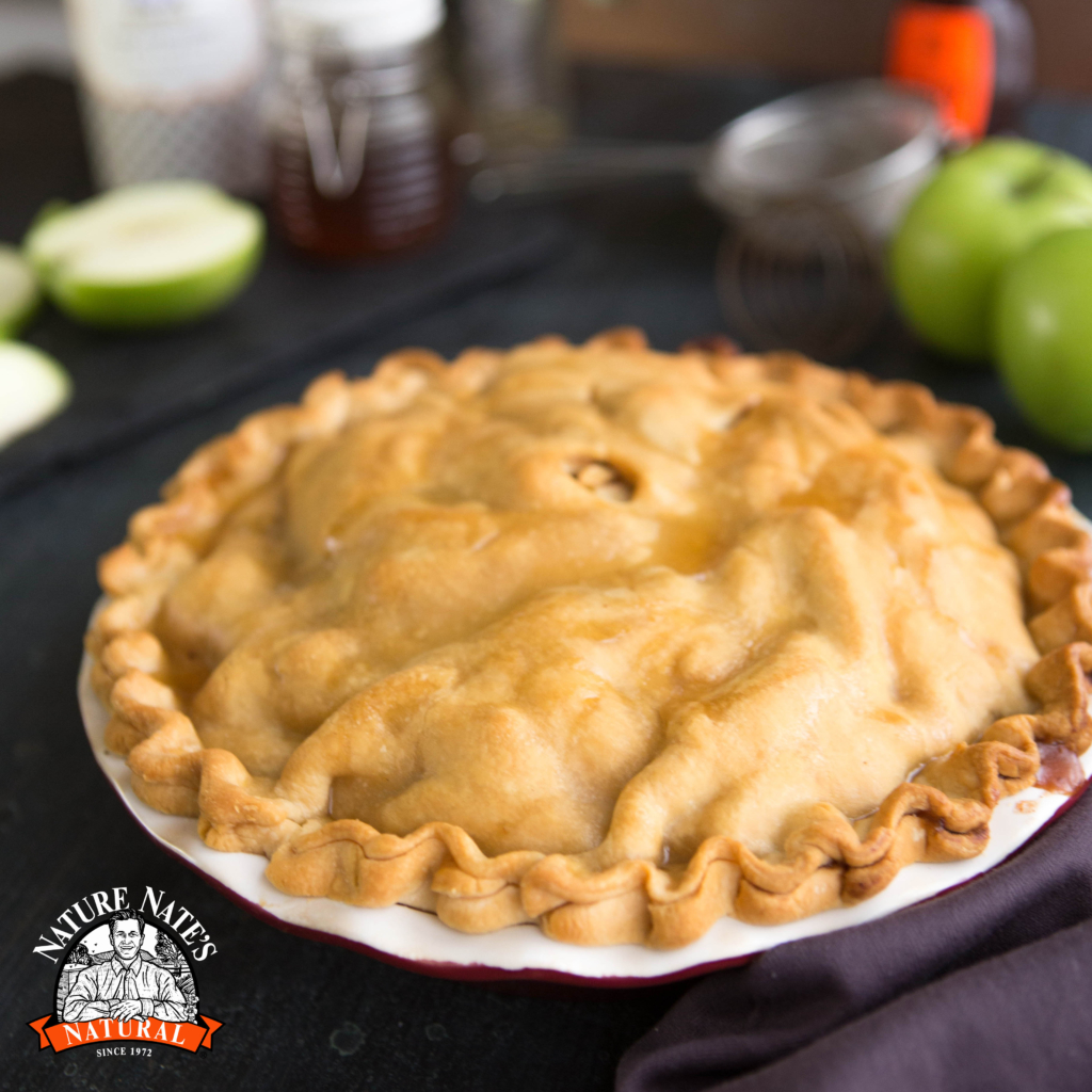 Golden pie on a plate, Nature Nate's logo, green apples background, cozy kitchen setting.