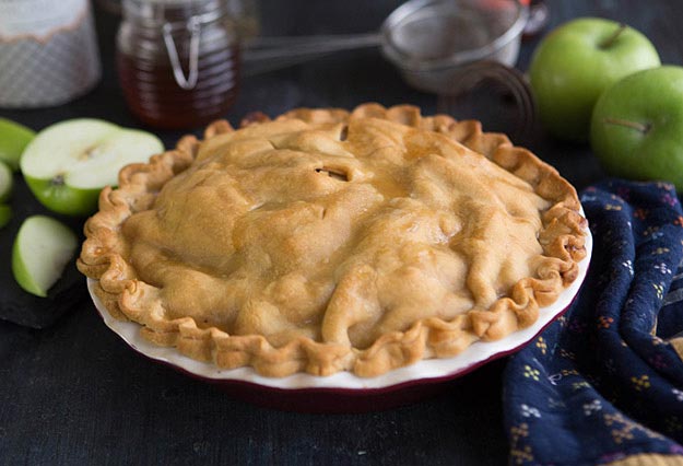 Freshly baked apple pie with apples, honey jar and cloth in the background.