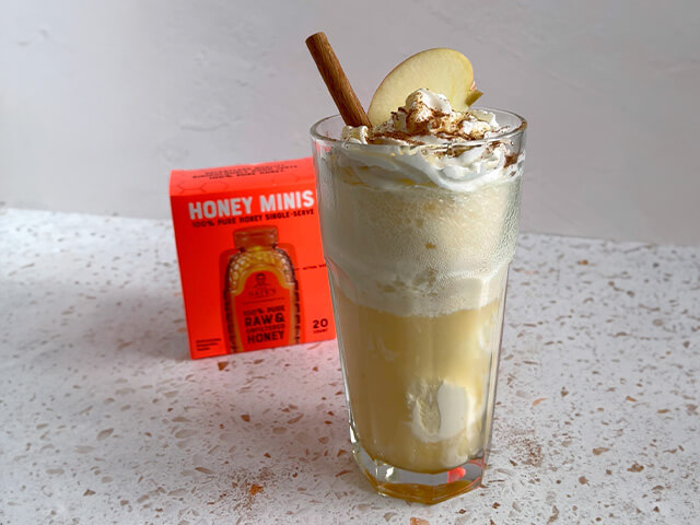 Tall glass of apple cider and ice cream. Topped with whipped cream, cinnamon, and apple slice with cinnamon stick garnish.