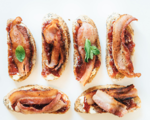 Assorted toasts topped with fruit spread and crispy bacon with fresh mint garnish displayed on a clean white background. Assorted toasts topped with fruit spread and crispy bacon with fresh mint garnish displayed on a clean white background.