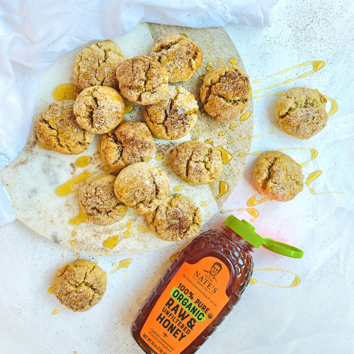 Cookies drizzled with honey next to a bottle of Nate’s organic honey on a white surface.
