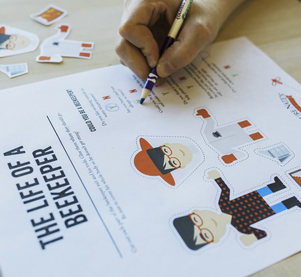 A close-up of a hand filling out a beekeeper's educational activity sheet with illustrations and text. 