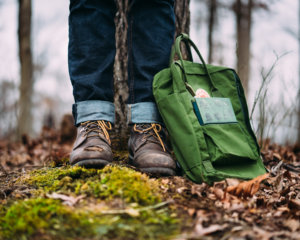 Hiking boots and green backpack in a forest setting.