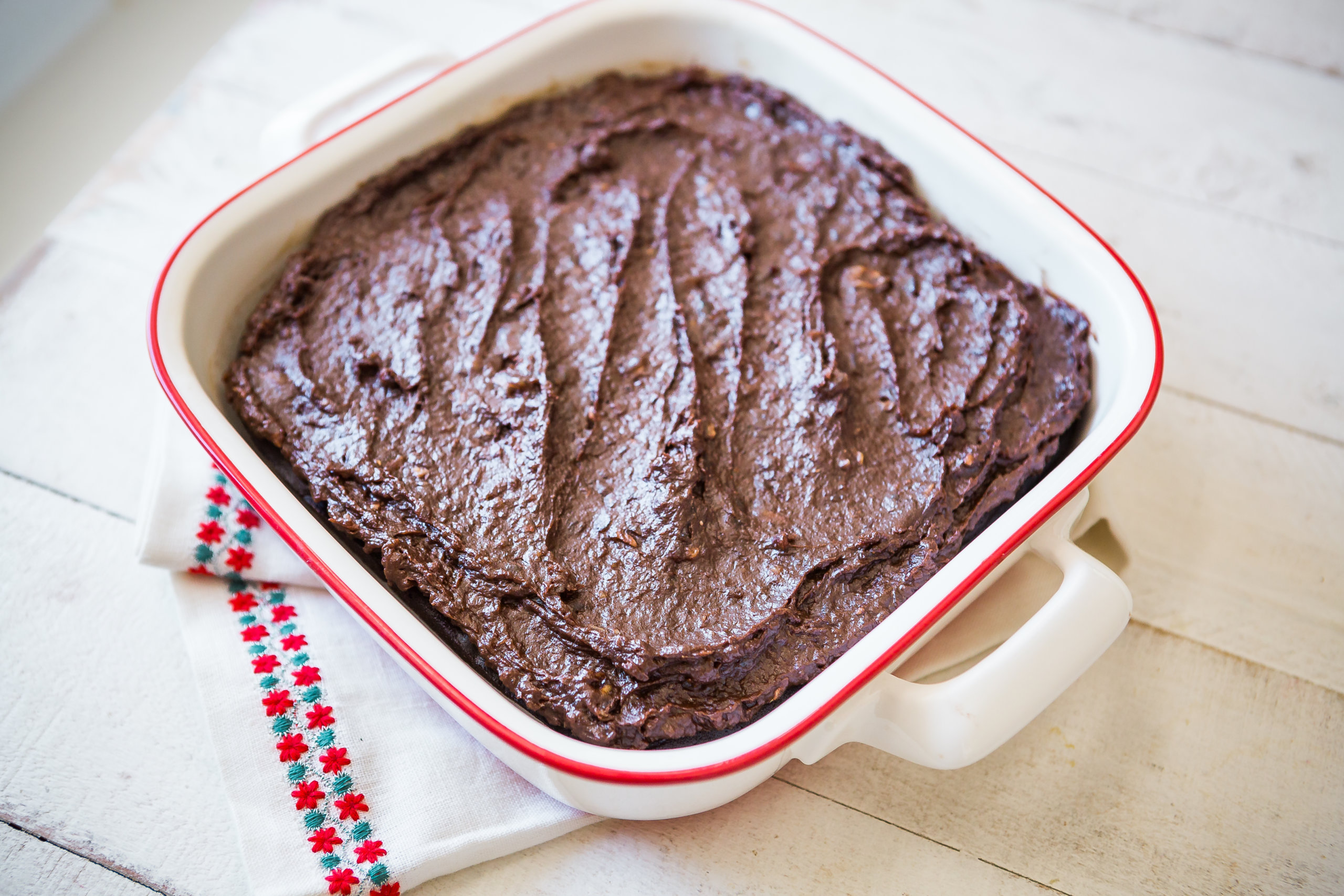 brownies topped with chocolate icing in red-rimmed white baking dish