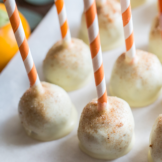Pumpkin spice cake pops with white icing and cinnamon, striped straws as sticks.