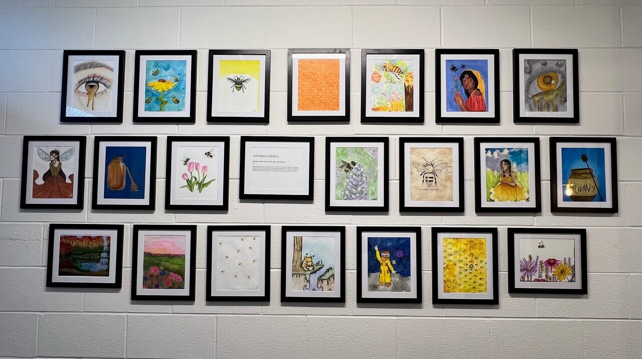 Twenty-two honey/sweetener themed works of art. All are framed in black and hung on a white wall.