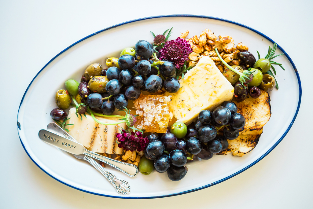 Cheese platter with grapes, crackers, nuts and honey on an oval plate.