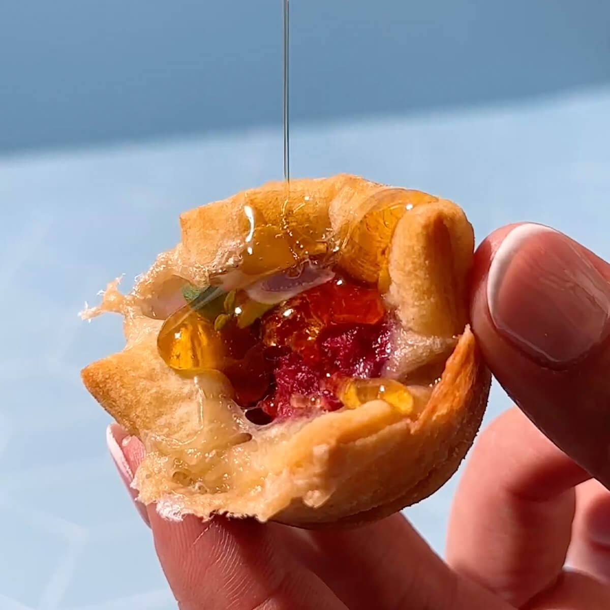 Drizzling Nate’s honey on a crescent roll bite with brie held between fingers.