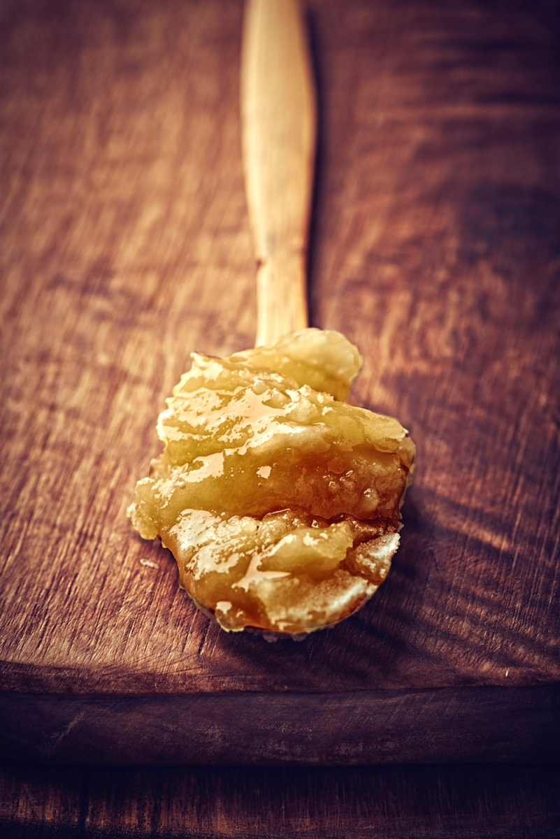 Spoonful of crystallized honey on a wooden background.