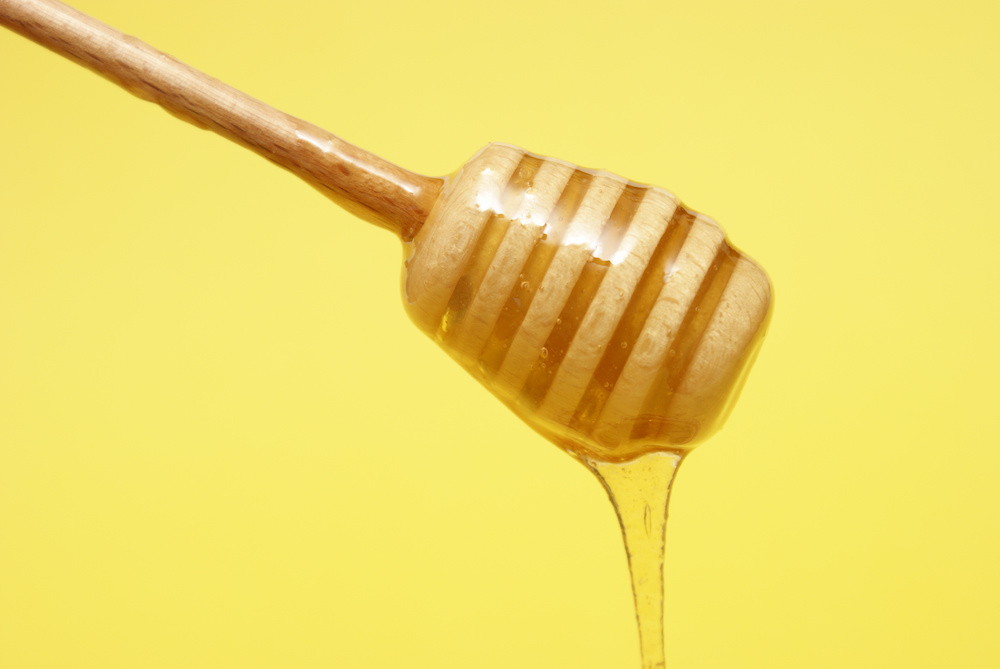 Honey dripping from a dipper on a yellow background.