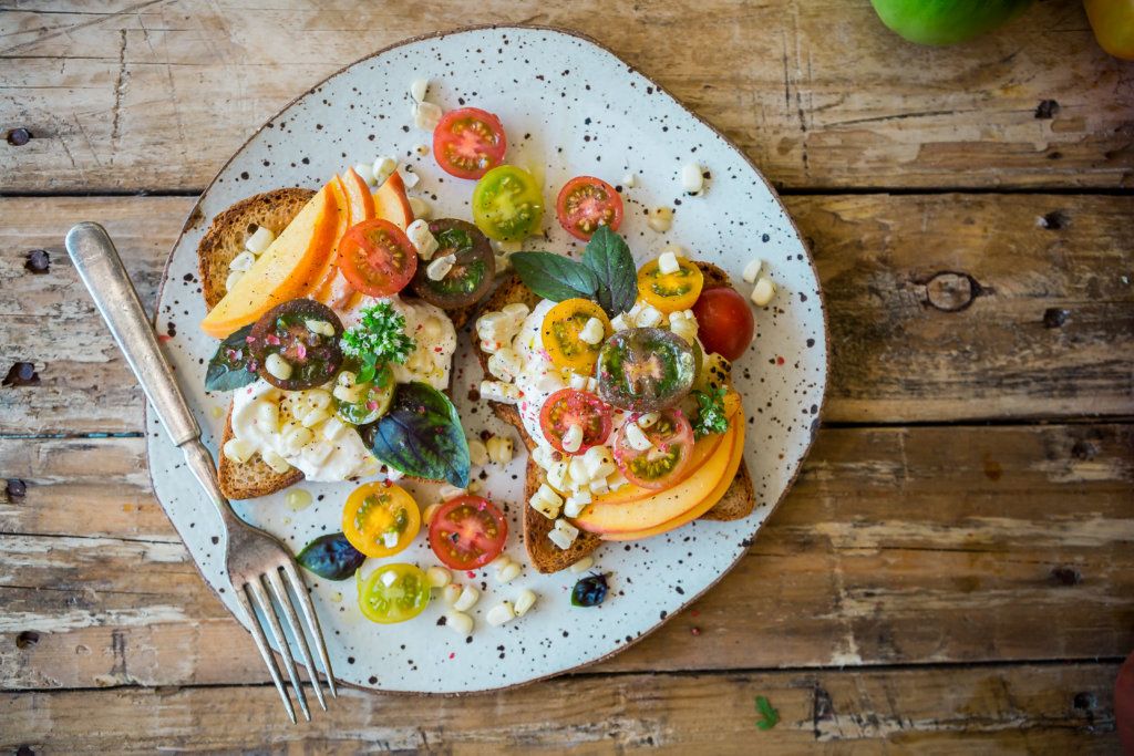 Open-faced sandwich with heirloom tomatoes, peach slices and burrata on speckled plate.