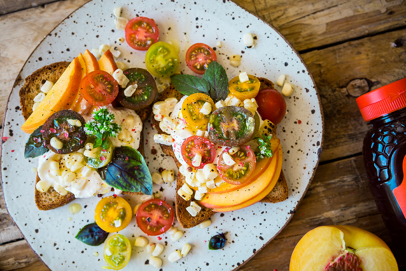 Open-faced sandwiches with various toppings like cheese, tomatoes, and herbs on a plate, next to Nate's honey bottle.