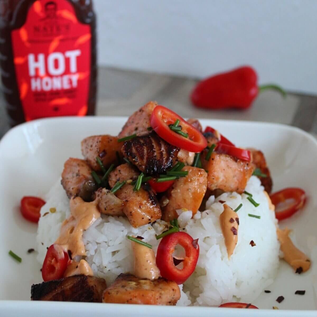 Firecracker Salmon Bites cooked with Nate’s Hot Honey on a bed of white rice garnished with chives and red chili peppers.
