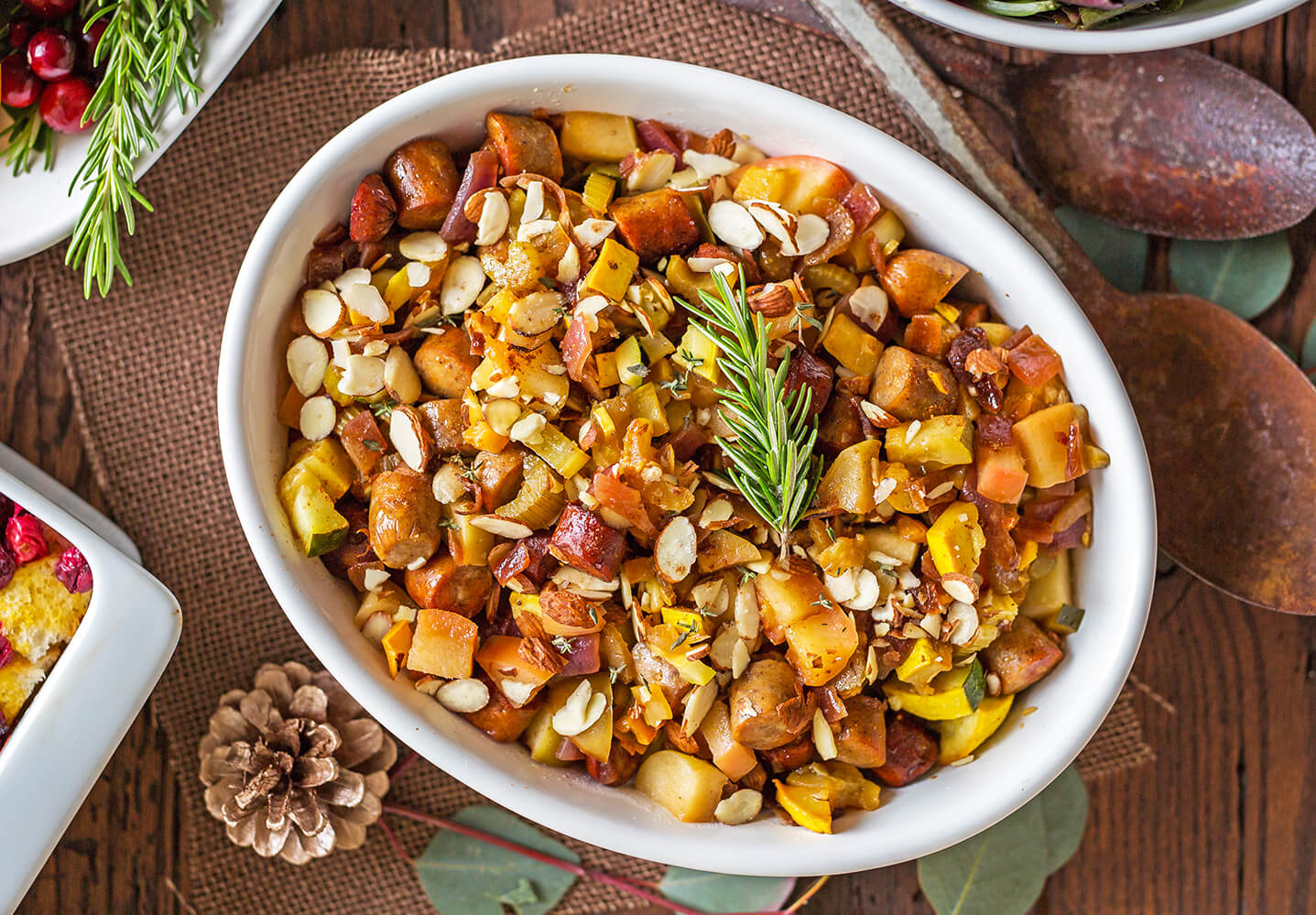 A roasted root vegetable dish with diced sweet potatoes, carrots, and garnished with chopped nuts and a sprig of rosemary.