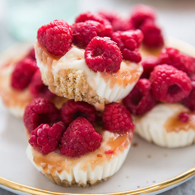Mini cheesecakes topped with fresh raspberries and drizzled with honey, presented on a gold-rimmed plate.