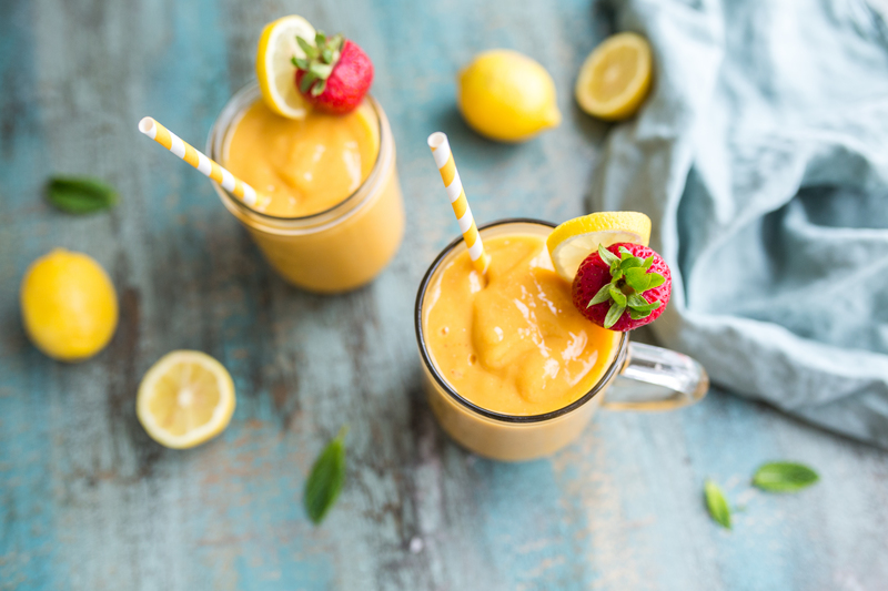 Strawberry mango smoothies with straws, lemons, and a blue cloth on a textured table.