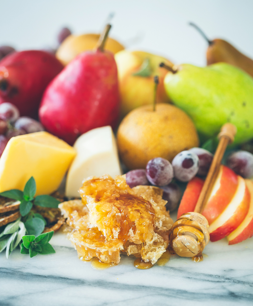 Assorted fruits with cheese and honeycomb on marble.