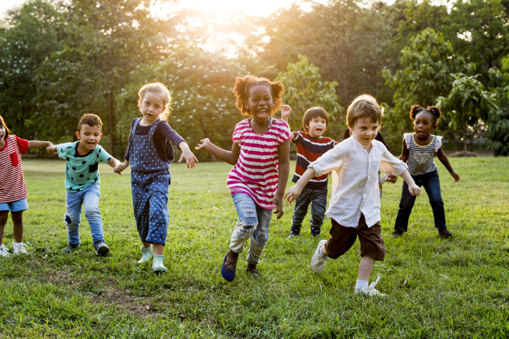 Children running on grass, sunlight filtering through trees, joy and movement captured.