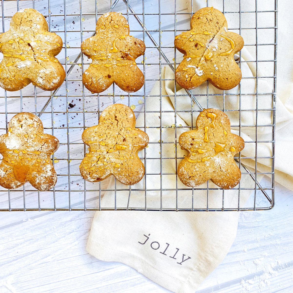 Gingerbread cookies made with honey on a wire rack over a napkin that reads JOLLY on a blue wooden surface.