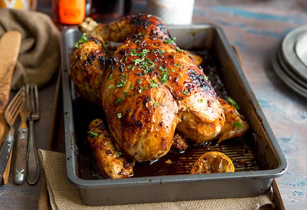 Roasted chicken in a pan, garnished with herbs, on a weathered table.