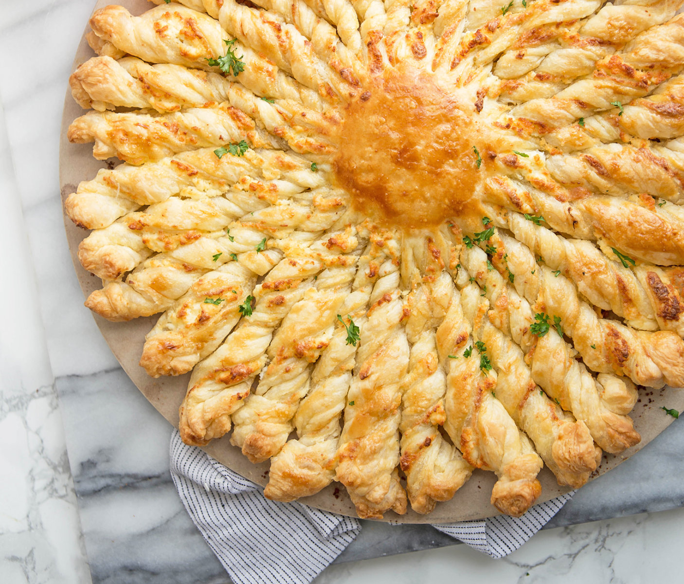 Cheesy pull-apart pastry with parsley and honey drizzle on a marble countertop with a striped napkin.