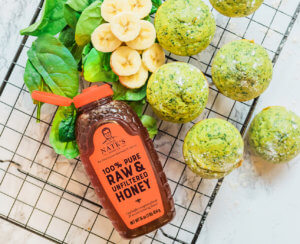 Spinach and banana muffins with a bottle of Nate's honey on a marble background.