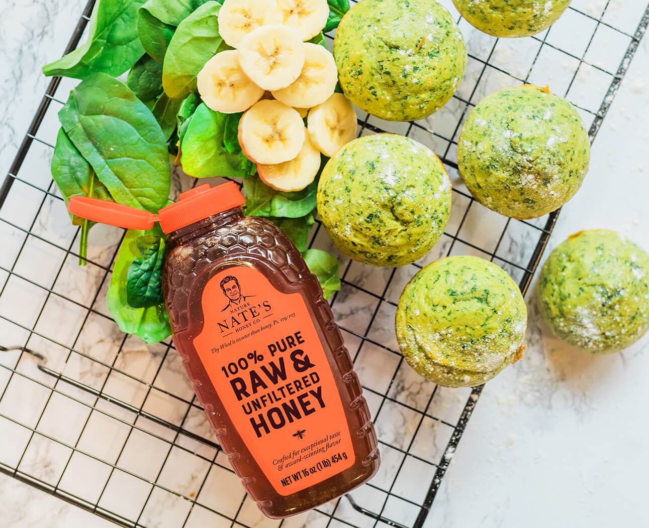 Spinach and banana muffins with honey bottle on marble background.