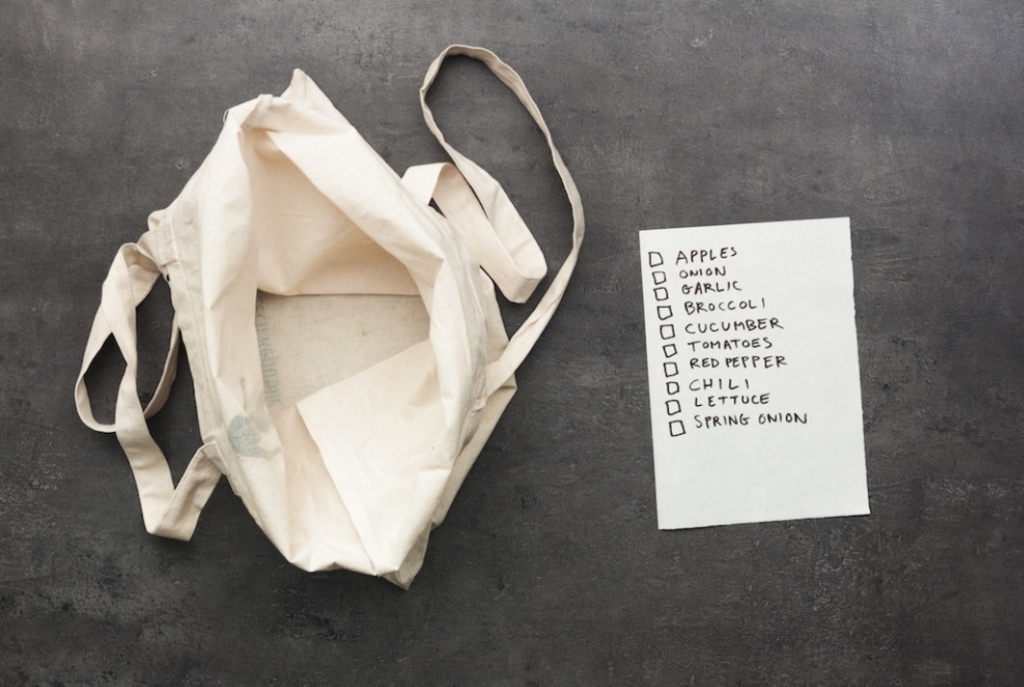 Empty tote bag with a grocery checklist on a gray background.