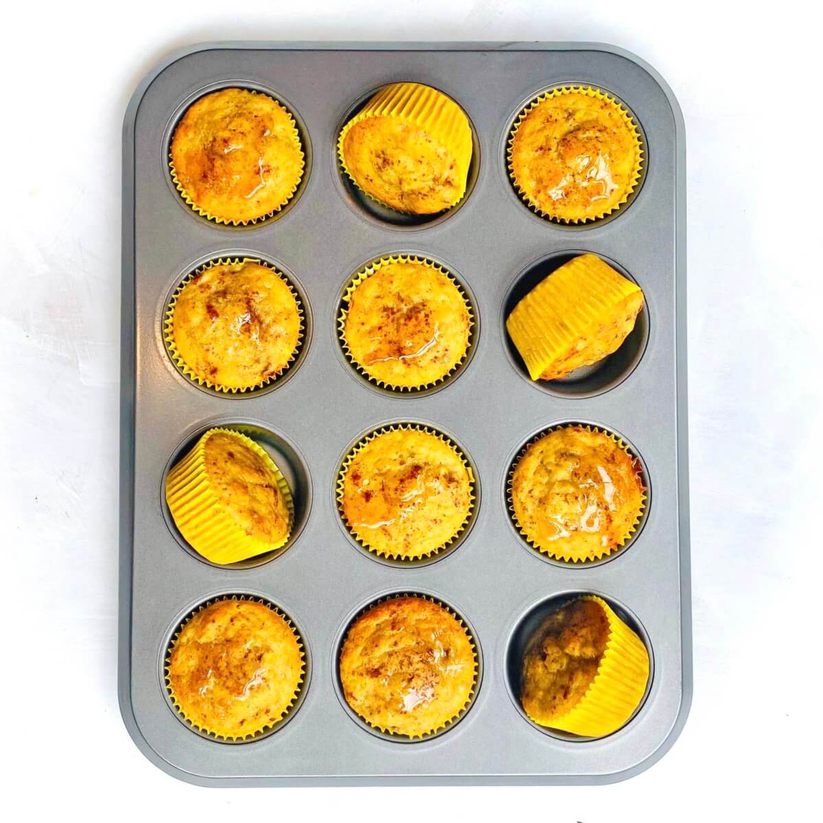 A tray of honey banana muffins in yellow liners, with one muffin tilted to show its moist interior.