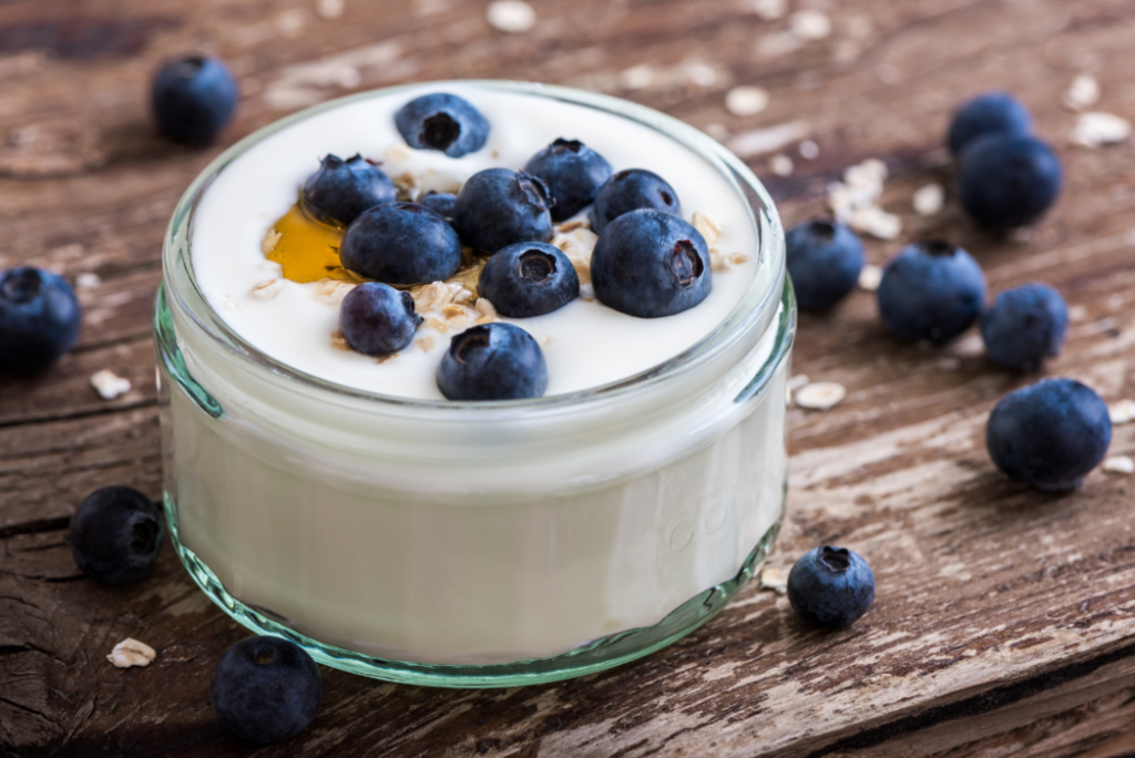 A bowl of yogurt with blueberries and a drizzle of honey on a rustic wooden surface.