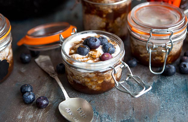 Overnight oats in jars topped with yogurt and blueberries on a textured surface.