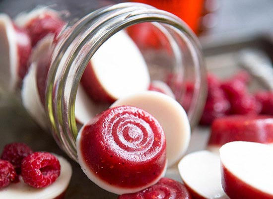 Raspberry gummy candies with white cream bottoms spill from jar on table.