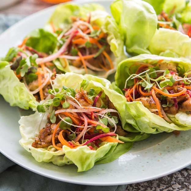 Asian-style chicken lettuce wraps with julienne vegetables and sprouts on a light ceramic plate.